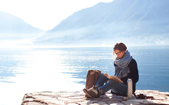 Woman wearing glasses reading book by the water